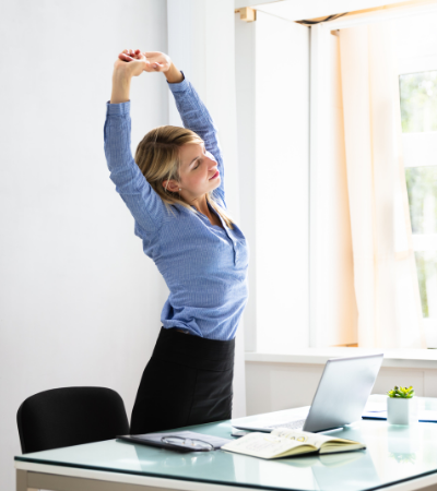 Tietokoneella työskentelevä nainen venyttelee käsiään ylös